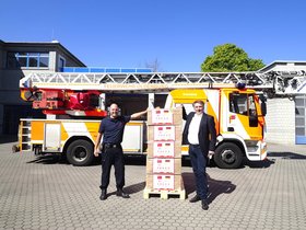 Feuerwehrmann Andreas Köker und Oberbürgermeister Jürgen Krogmann mit den Masken vor einem Feuerwehrauto. Foto: Sascha Stüber