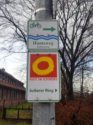 Beschilderung Hunteweg Radfernweg mit Richtungspfeil und Route um Oldenburg (gelber Kreis auf rotem Grund) mit Richtungspfeil und Schriftzug „äußerer Ring". Foto: Stadt Oldenburg