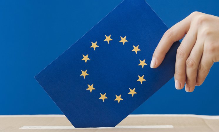 Hand steckt Europaflagge in eine Wahlurne. Foto: Freepik