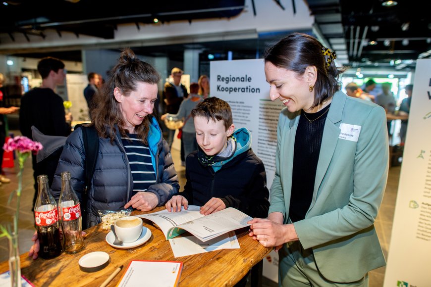 Ein Junge durchstöbert interessiert die Broschüre „ISEK Zukunft 2050“ mit seiner Mutter und einer Mitarbeiterin des Stadtplanungsamtes. Foto: Hauke-Christian Dittrich