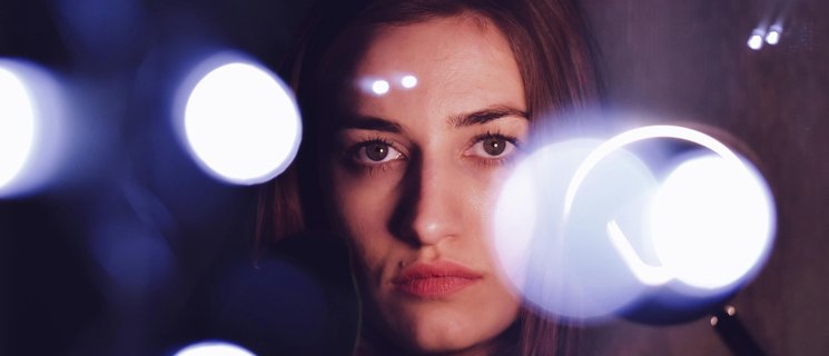 Gesicht einer Frau im Dunkeln, Lichtpunkte um sie herum. Foto: Dids/pexels