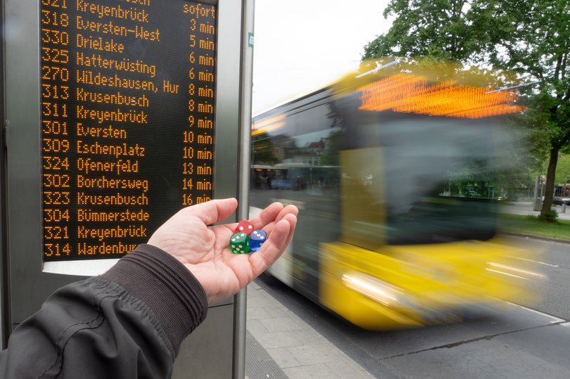 Eine Hand mit Würfeln und ein Bus an einer Bushaltestelle. Foto: Andreas Wulff/Franz Josef Wieczorek
