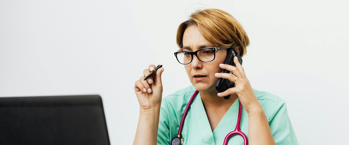 Eine Medizinerin sitzt mit Telefon und Stethoskop vor einem Computer. Foto: Karolina Grabowska/Pexels