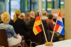 Ein Ständer mit deutscher und niederländischer Flagge. Im Hintergrund Teilnehmende eines Oldenburg-Groninger Treffens. Foto: Thorsten Helmerichs