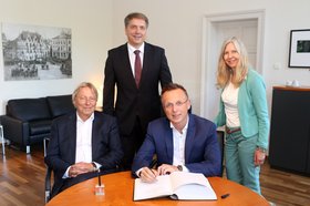 Peter den Oudsten und René Paas sitzen an einem Tisch, hinter ihnen stehen Oberbürgermeister Jürgen Krogmann und Bettina Fabich. Foto: Stadt Oldenburg
