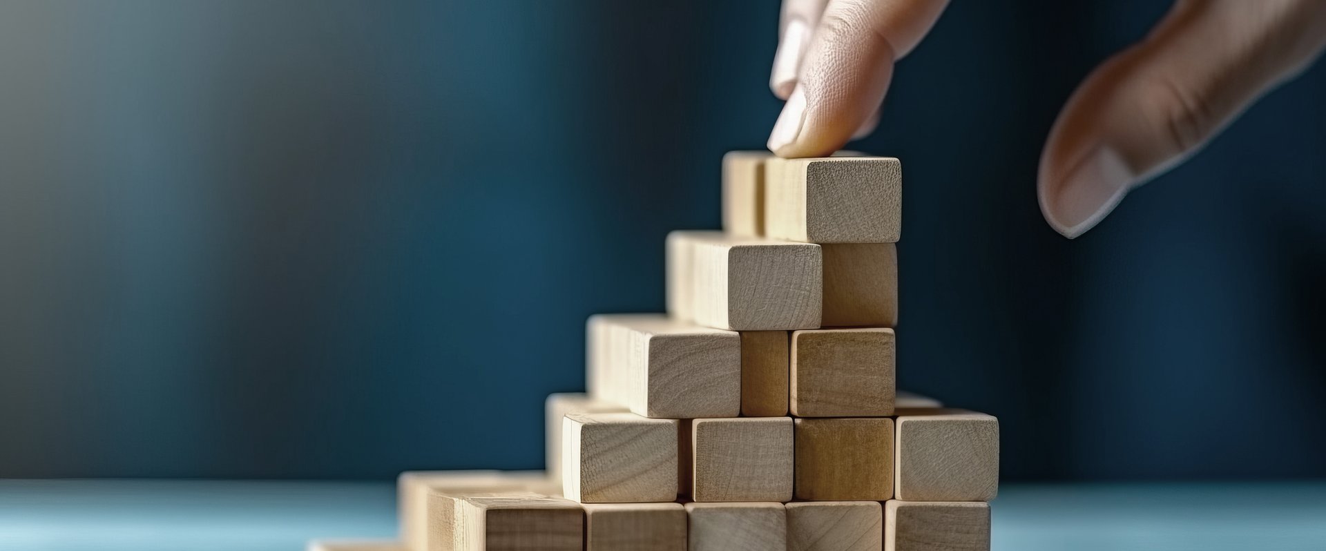 Hand baut eine Pyramide aus kleinen Holzwürfeln. Foto: Valentyn640/AdobeStock