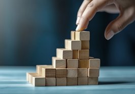 Hand baut eine Pyramide aus kleinen Holzwürfeln. Foto: Valentyn640/AdobeStock