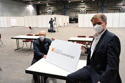 Der Leiter der Feuerwehr, Michael Bremer (links), und Oberbürgermeister Jürgen Krogmann mit einem Schild mit dem Logo des Impfzentrums. Foto: Sascha Stüber