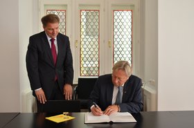 Oberbürgermeister Jürgen Krogmann steht neben dem Stuhl, auf dem Groningens Bürgermeister Peter den Oudsten sitzt und sich in das Gästebuch einträgt. Foto: Stadt Oldenburg