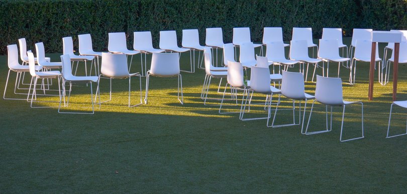 Zu sehen sind ungefähr vierzig weiße Stühle auf einer grünen, beleuchteten Wiese, die zu einander ausgerichtet aufgestellt sind. Foto: Rainer Sturm/pixelio.de