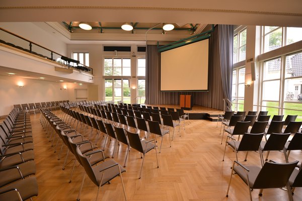 Veranstaltungssaal PFL, Blick von der hinteren rechten Ecke auf die Bühne mit heruntergelassener Leinwand. Foto: Jörg Hemmen