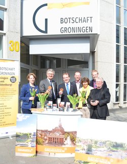 Pressekonferenz zur Botschaft Groningen: Im Hintergrund ist das Logo zu sehen, auf einem Tresen stehen Tulpen, die Beteiligten halten Sirupwaffeln in der Hand. Foto: Stadt Oldenburg