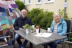 Zwei Personen sitzen am Tag der Nachbarn draußen am Tisch und lächeln in die Kamera. Foto: Carsten Lienemann