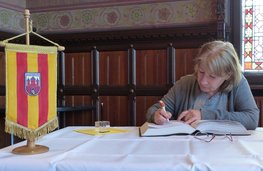 Reiseleiterin Gadzhieva Dilbara Abdulajevna trägt sich in das Gästebuch der Stadt ein, neben ihr steht eine kleine Fahne mit rot-gelben Streifen und dem Wappen Oldenburgs. Foto: Stadt Oldenburg
