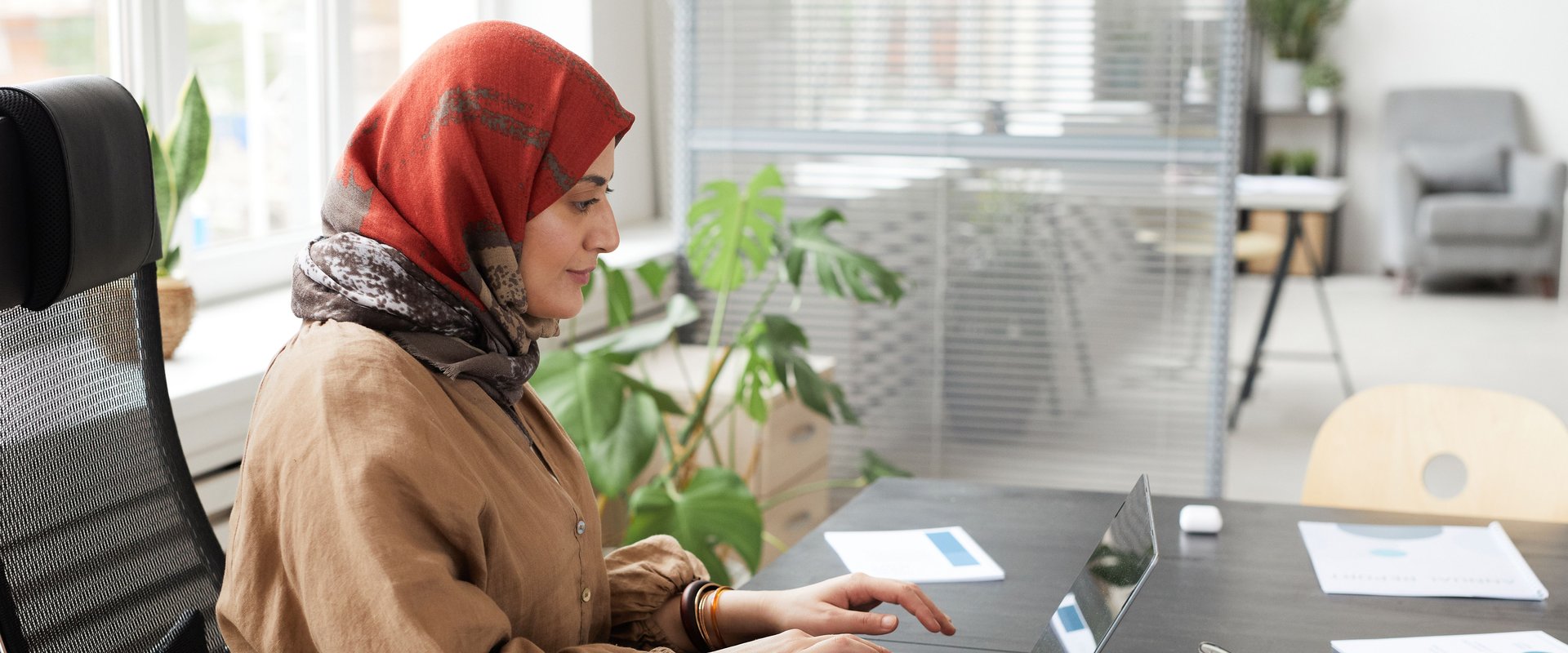 Eine Frau mit rotem Hijab arbeitet in einem modernen Büro am Laptop. Foto: cedric fauntleroy/pexels