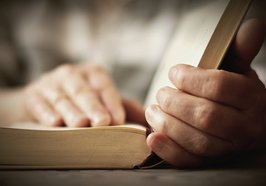 Aus einem geöffneten Buch wird vorgelesen und die Hände liegen auf einer Buchseite. Foto: congerdesign/Pixabay