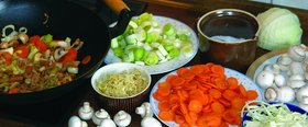 Links im Bild ein Wok mit Gemüse, daneben stehen Teller und Schüsseln mit geschnittenem Gemüse. Foto: Heidrun Schneider/Pixelio.de