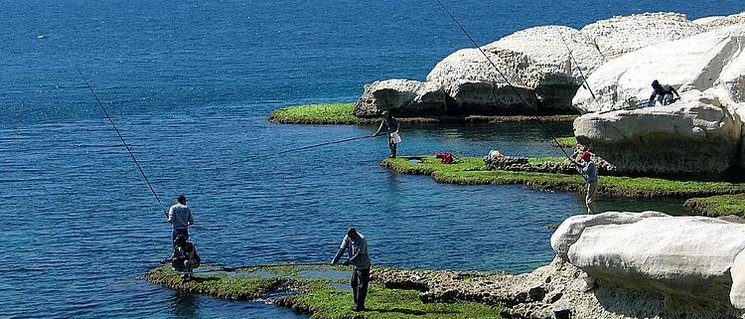 Blaues Meer, blauer Himmel und weiße Felsen. Am Ufer stehen zwei Menschen und angeln. Foto: Matte Asher Regional Council