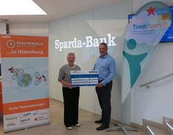Hermann Kruse, Filialleiter der Sparda-Bank West eG, überreicht den Scheck für das Erreichen des siebten Etappenziels an Antje Möhrmann, Vorstand TrostReich e.V. Foto: Stadt Oldenburg