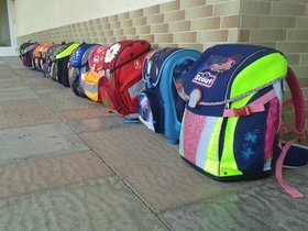 Eine Reihe bunter Schulranzen steht entlang einer Wand. Foto: Volker Oerschkes/pixelio