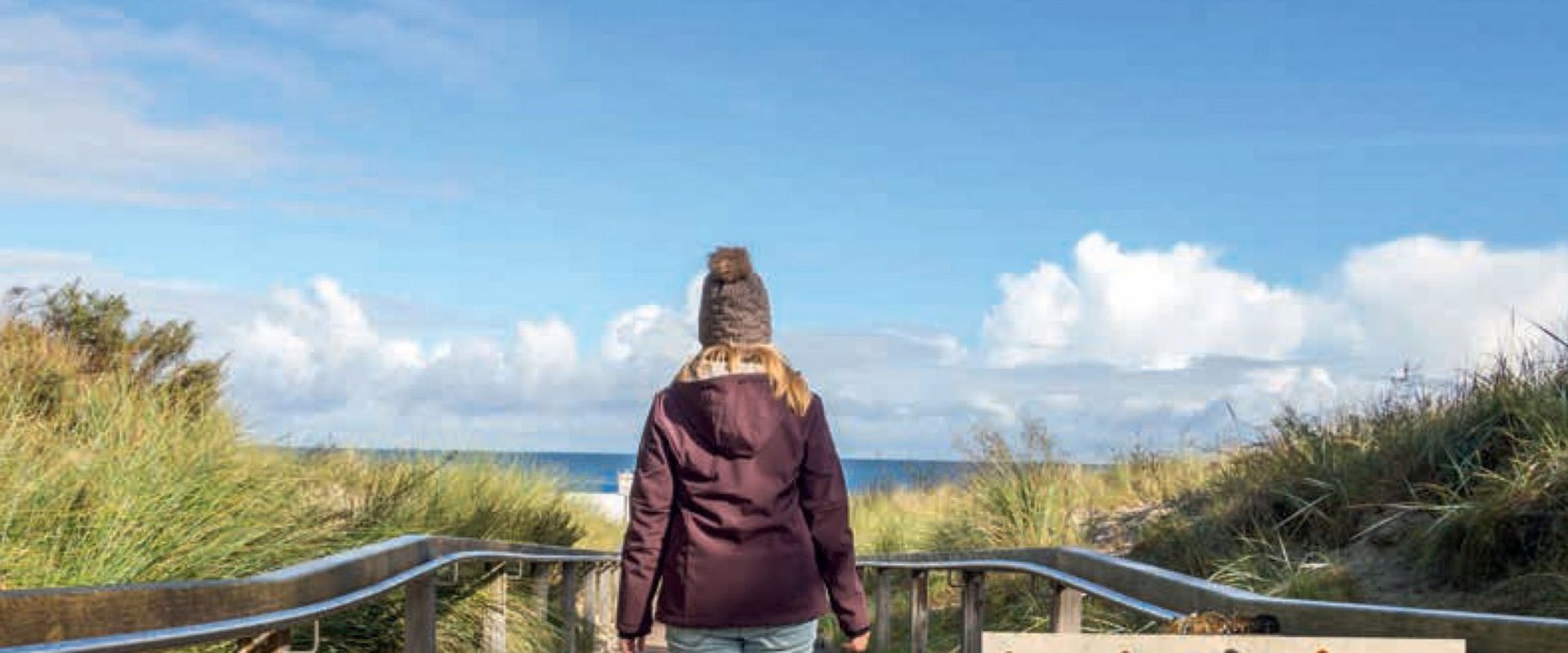 Titel Zukunft gestalten, junge Frau schaut von den Dünen aufs Meer hinaus. Foto: Animaflora PicsStock/AdobeStock