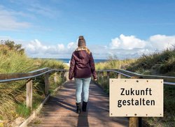 Titel Zukunft gestalten, junge Frau schaut von den Dünen aufs Meer hinaus. Foto: Animaflora PicsStock/AdobeStock