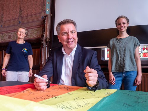 Oberbürgermeister Jürgen Krogmann unterschreibt die Regenbogenfahne des NaUnd e.V. Mit dabei Inka Jakobs (links) und Kim König. Foto: Sascha Stüber