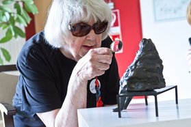 Ältere Frau betrachtet Kunstwerk der Artothek mit Lupe
