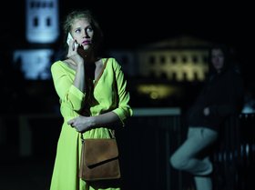 Eine Frau steht alleine telefonierend nachts auf der Straße, im Hintergrund lehnt ein Mann an einem Geländer. Foto: Photographee.eu/Adobe Stock