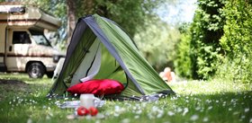 Ein Zelt steht auf einer Wiese. Im Hintergrund sieht man ein Wohnmobil. Foto: Peter Atkins/Fotolia.com