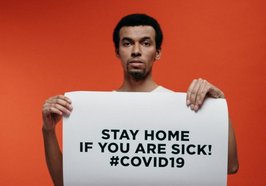 Mann mit Schild „Bleib Zuhause, wenn du krank bist! #Covid19. Foto: cottonbro/Pexels