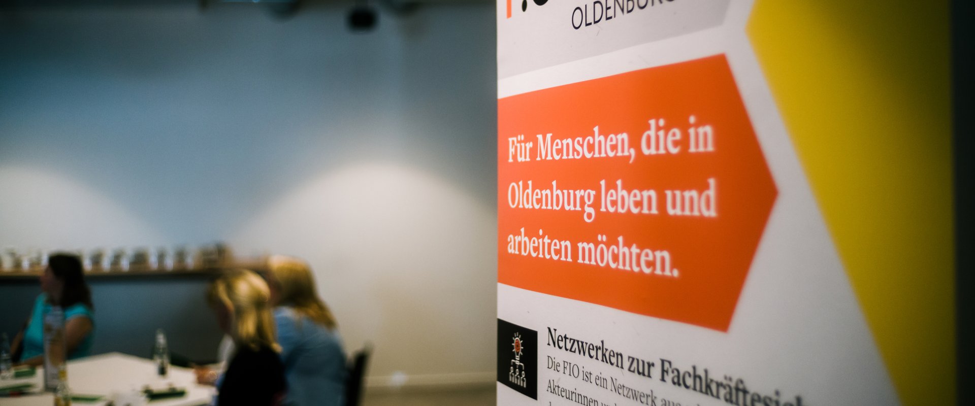 Roll-up der Fachkräfte-Initiative Oldenburg (FIO), im Hintergrund Gruppenarbeitsphase während eines Fachkräfte-Forums. Foto: Jörn Tempel