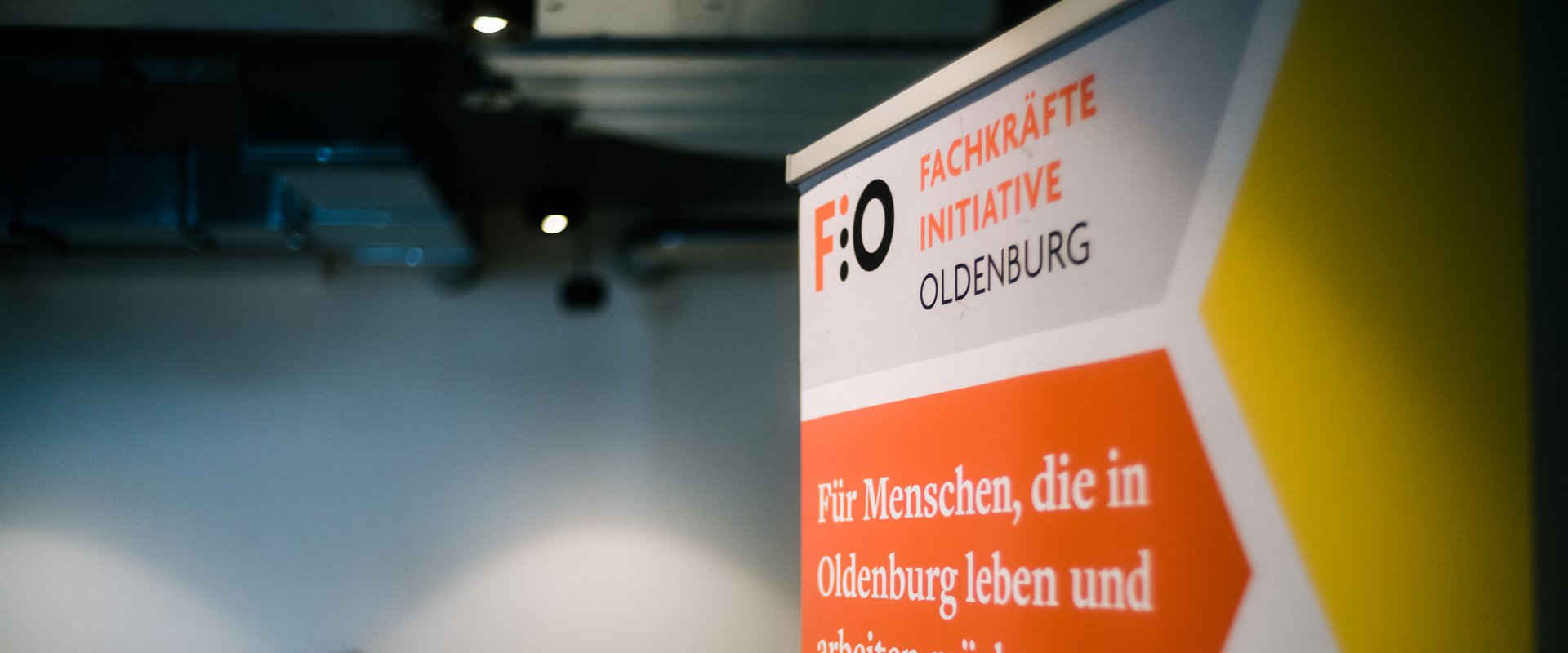 Roll-up der Fachkräfte-Initiative Oldenburg (FIO), im Hintergrund Gruppenarbeitsphase während eines Fachkräfte-Forums. Foto: Jörn Tempel