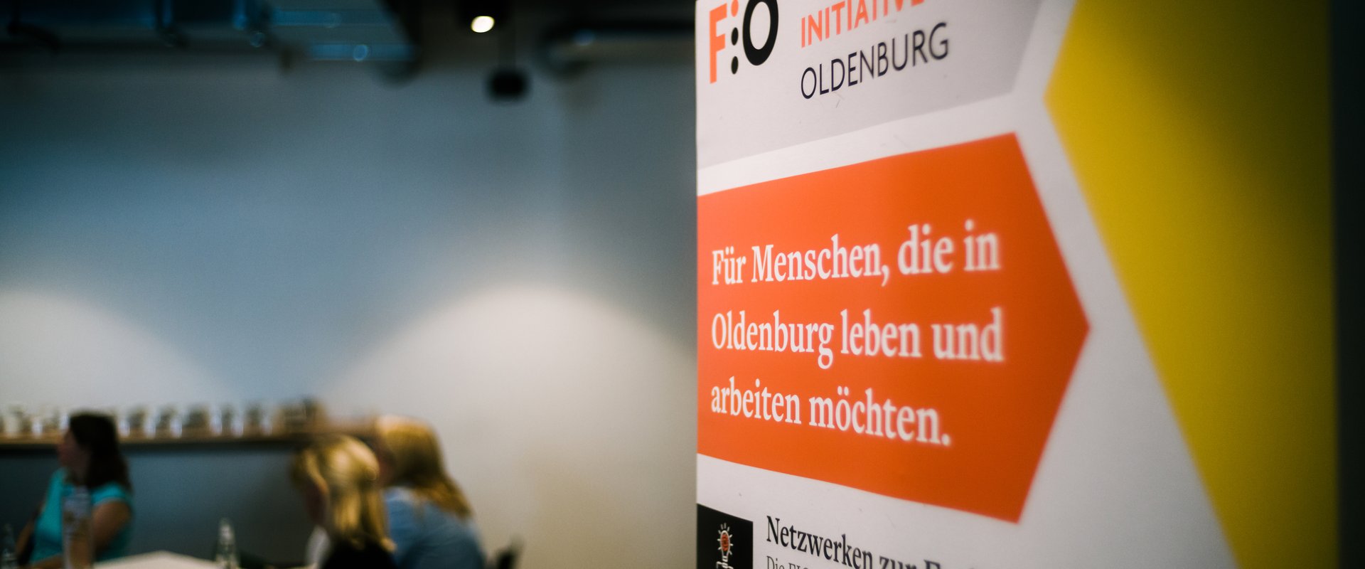 Roll-up der Fachkräfte-Initiative Oldenburg (FIO), im Hintergrund Gruppenarbeitsphase während eines Fachkräfte-Forums. Foto: Jörn Tempel