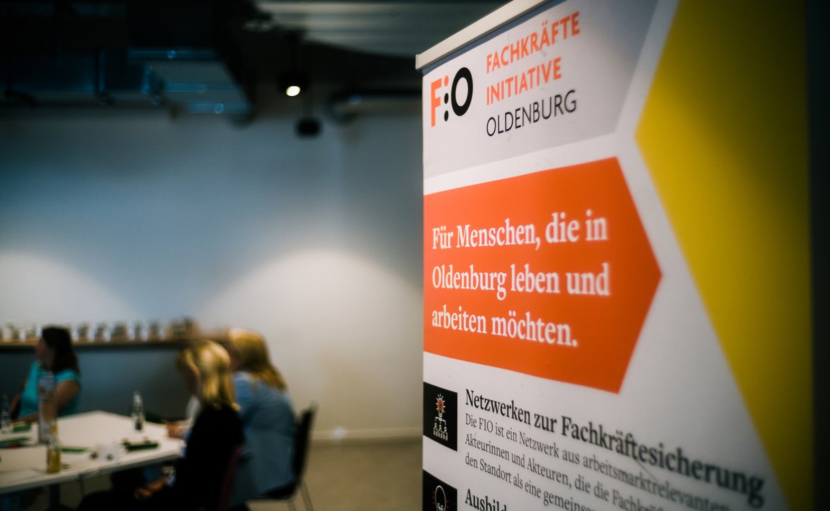 Roll-up der Fachkräfte-Initiative Oldenburg (FIO), im Hintergrund Gruppenarbeitsphase während eines Fachkräfte-Forums. Foto: Jörn Tempel
