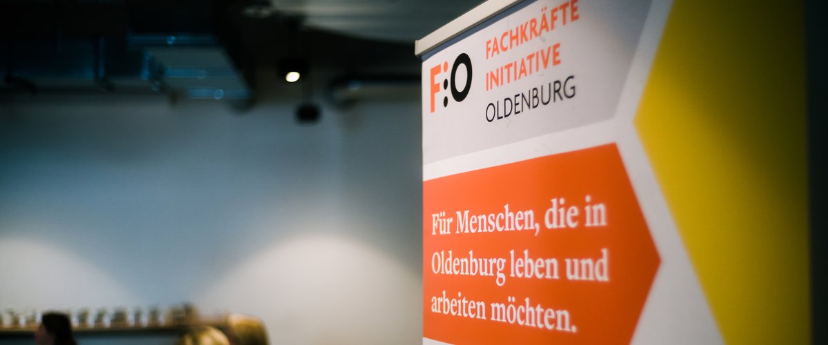 Roll-up der Fachkräfte-Initiative Oldenburg (FIO), im Hintergrund Gruppenarbeitsphase während eines Fachkräfte-Forums. Foto: Jörn Tempel