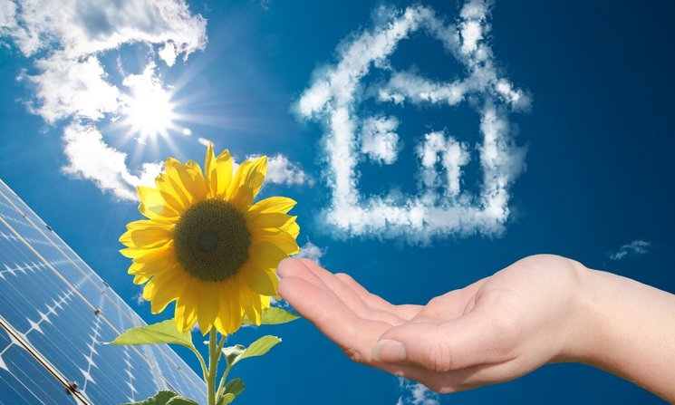 Solarmodule, Sonnenblume, Haus aus Wolken und Hand vor blauem Himmel. Foto: Franz/AdobeStock