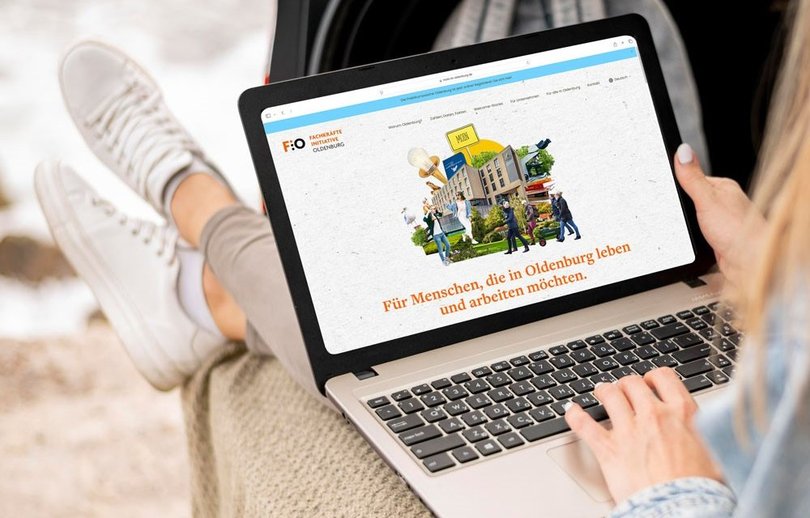 Junge Frau mit Laptop auf den Beinen surft auf der Homepage von „Moin in Oldenburg“. Foto: Superidee