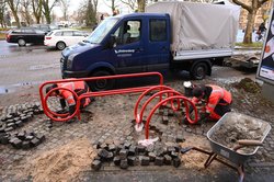 Arbeiter installieren am Pferdemarkt die „Tube Line“, Sitzbank und Fahrradstand zugleich. Foto: Jörg Hemmen Eine Baustelle, in der zwei Arbeiter eine Konstruktion aus rot lackiertem Stahlrohr im Boden verankert. Foto: Jörg Hemmen