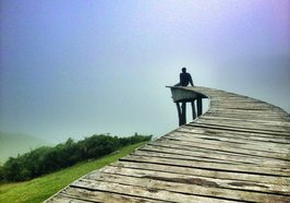 Ein Mann sitzt alleine auf einem Holzsteg und schaut in die Weite. Foto: ericsan/AdobeStock