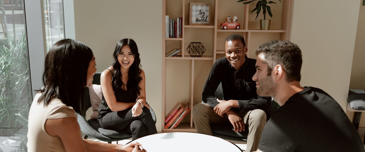 Vier junge Menschen unterhalten sich am runden, weißen Tisch. Foto: RDNE Stock Project/Pexels