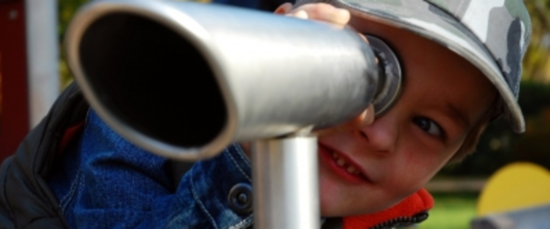 Ein Junge schaut auf einem Spielplatz durch ein Fernrohr. Foto: erysipel/Pixelio