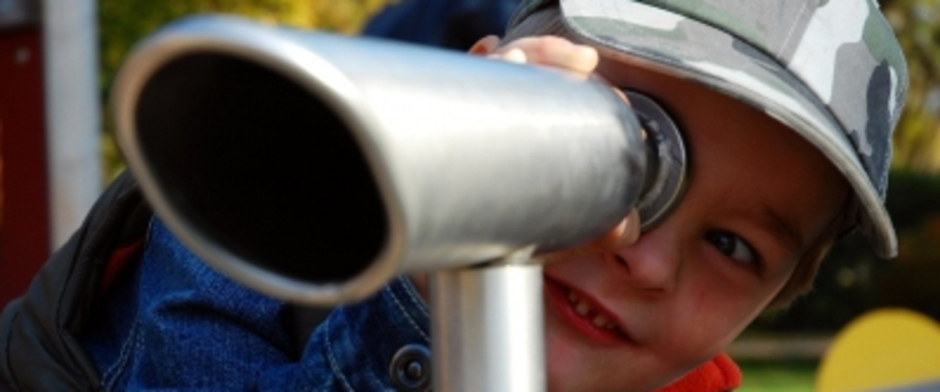 Ein Junge schaut auf einem Spielplatz durch ein Fernrohr. Foto: erysipel/Pixelio