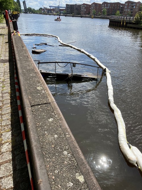 Nachdem der Katamaran im Oldenburger Hafen abgebrannt ist, ist das Boot zwei Tage später gesunken. Zu sehen ist nur noch die Ölsperre der Feuerwehr. Foto: Stadt Oldenburg Foto: Stadt Oldenburg