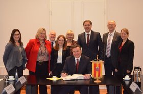 Kevin Davis (sitzend) trägt sich in das Gästebuch der Stadt ein, um ihn herum stehen Mitglieder der Delegation aus Kingston. Foto: Stadt Oldenburg