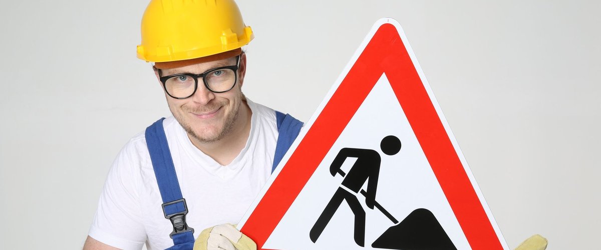 Mann mit Bauarbeiterhelm hält ein Baustellenschild in den Händen. Foto: Tim Reckmann/Pixelio