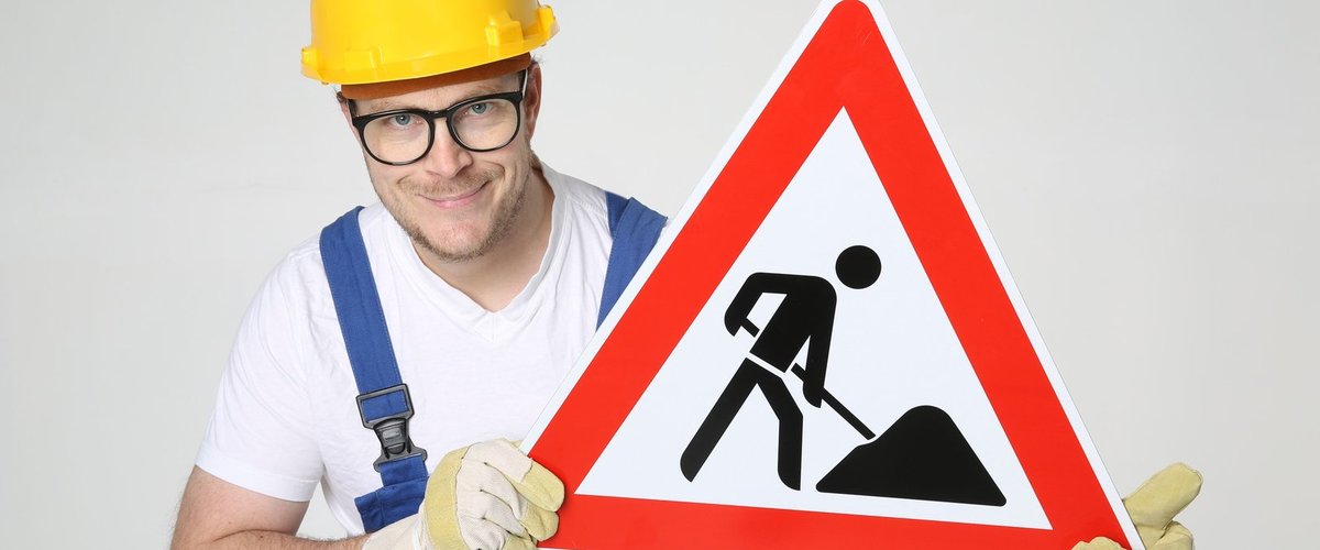 Mann mit Bauarbeiterhelm hält ein Baustellenschild in den Händen. Foto: Tim Reckmann/Pixelio