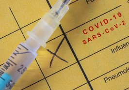 Nahaufnahme einer Spritze auf einem gelben Impfausweis mit Covid-19-Impfangabe. Foto: Benedikt/AdobeStock