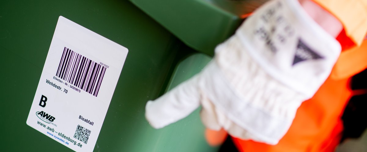 Die Hand eines Müllwerkers zeigt auf eine Biotonne des Abfallwirtschaftsbetriebs Stadt Oldenburg. Foto: Hauke-Christian Dittrich