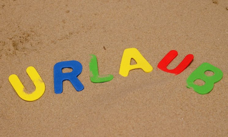 Bunte Buchstaben mit der Aufschrift „URLAUB“ liegen im Sand. Foto: S. Hofschlaeger/Pixelio 
